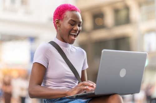 Happy african woman using the laptop on the street
