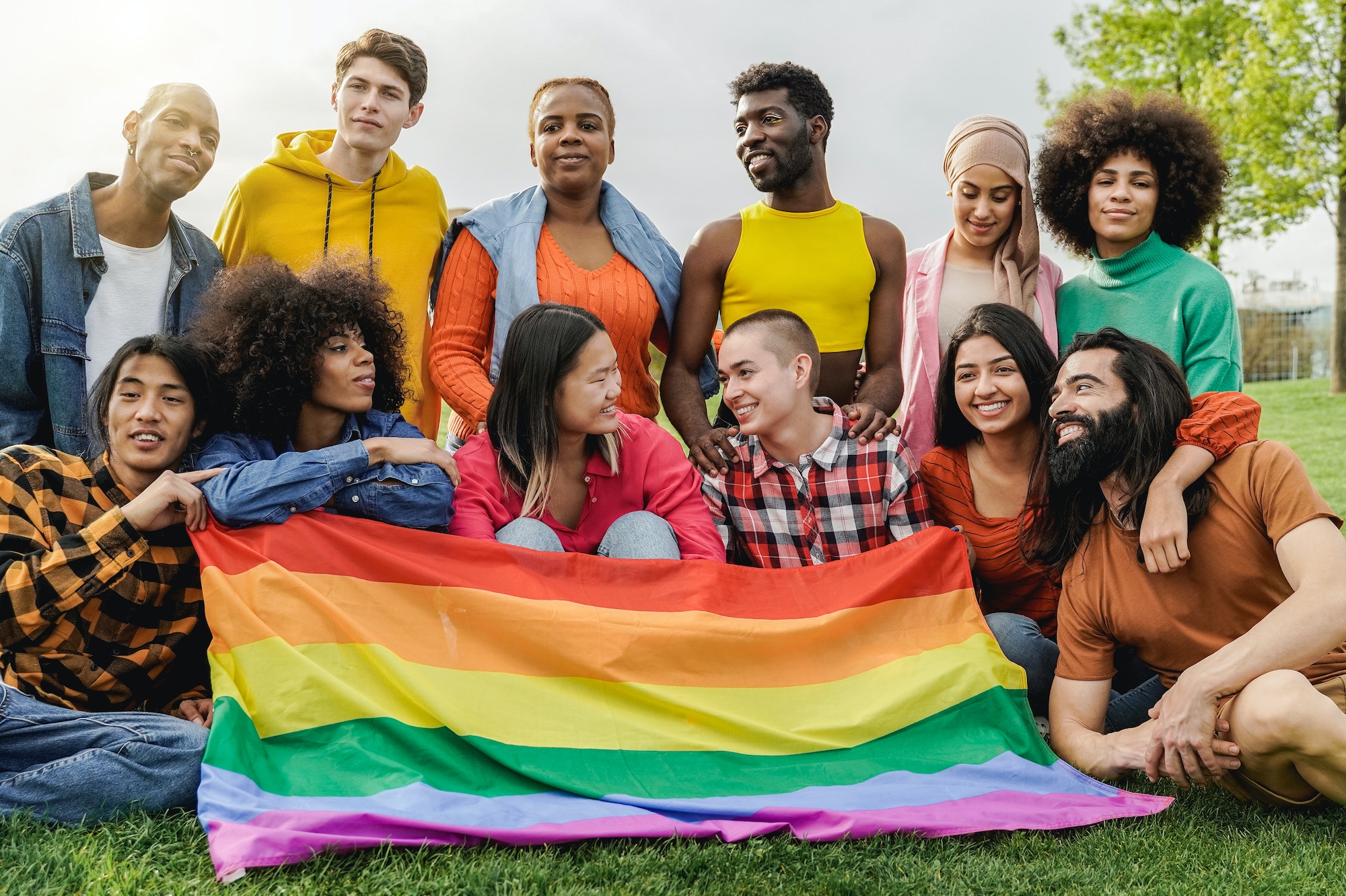 Happy diverse friends holding LGBT rainbow flag having fun together outdoors - Focus on bald girl